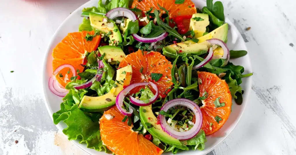 A plate of citrus salad with avocado slices and mixed greens