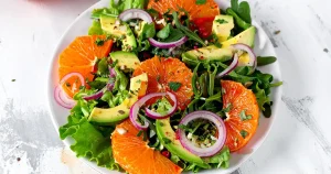 A plate of citrus salad with avocado slices and mixed greens