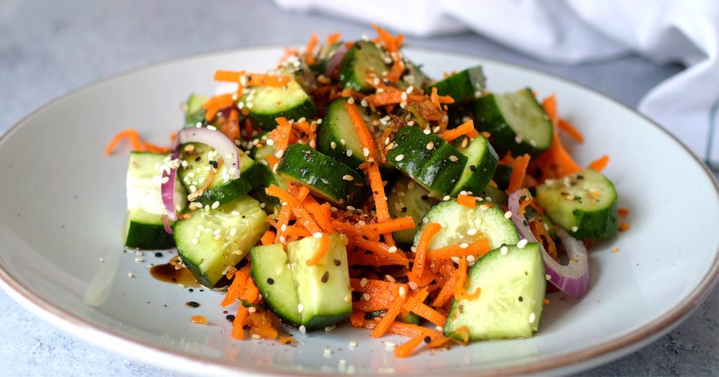 A plate of salad with sliced cucumber, grated carrots and sesame seeds