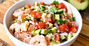 A bowl of shrimp ceviche with tomatoes, avocado, and cucumber
