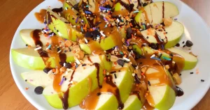 Caramel Apple Nachos, drizzled with caramel and chocolate sauce, sprinkled with mini chocolate chips, chopped peanuts, toffee bits, and Halloween sprinkles.