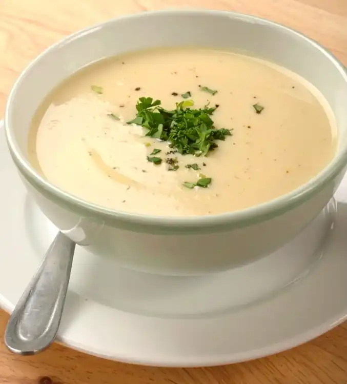 A bowl of garlic soup, topped with chopped parsley